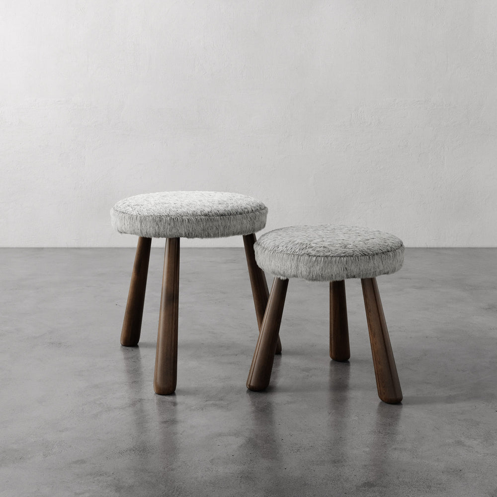 Lemieux et Cie Madeleine Leather Stool in grey with tapered legs, stackable ottomans on polished concrete floor against textured plaster walls.