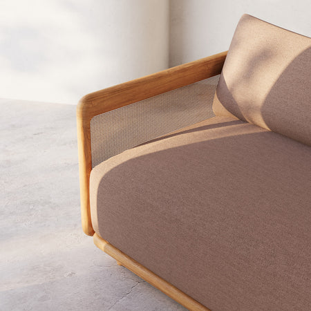 Lemieux et Cie Dock Teak Swivel Lounge Chair with woven cane panel and neutral upholstery, angled view against white plaster walls on concrete floor.
