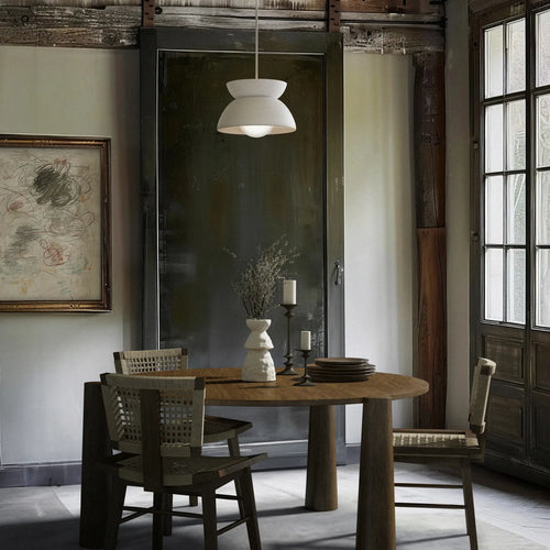 Lemieux et Cie Jeanneret Dining Chairs in teakwood with hand-woven cane, positioned around a round wood table in a dining room with neutral walls and dark mirrored cabinet.