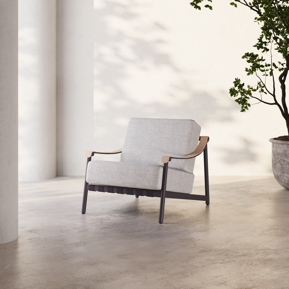 Lemieux et Cie Hudson Lounge Chair with light gray upholstery and dark frame, shown on concrete flooring in a sunlit white-walled room.
