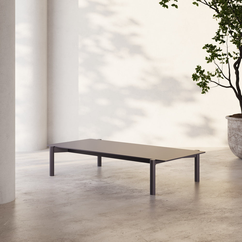 Lemieux et Cie Hudson 63" Rectangular Coffee Table, low-profile table with dark rectangular top and cylindrical legs, on concrete floors in soft daylight.