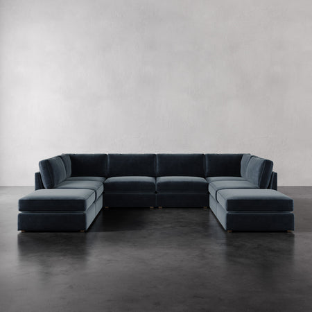 Lemieux et Cie Chanaux 8-Pc Sectional in charcoal gray, modular U-shaped sofa with dual ottomans on dark concrete floor, neutral plastered walls.