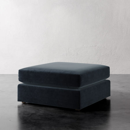 Lemieux Et Cie Chanaux Ottoman
 Dark gray ottoman on a reflective surface with a white textured wall background