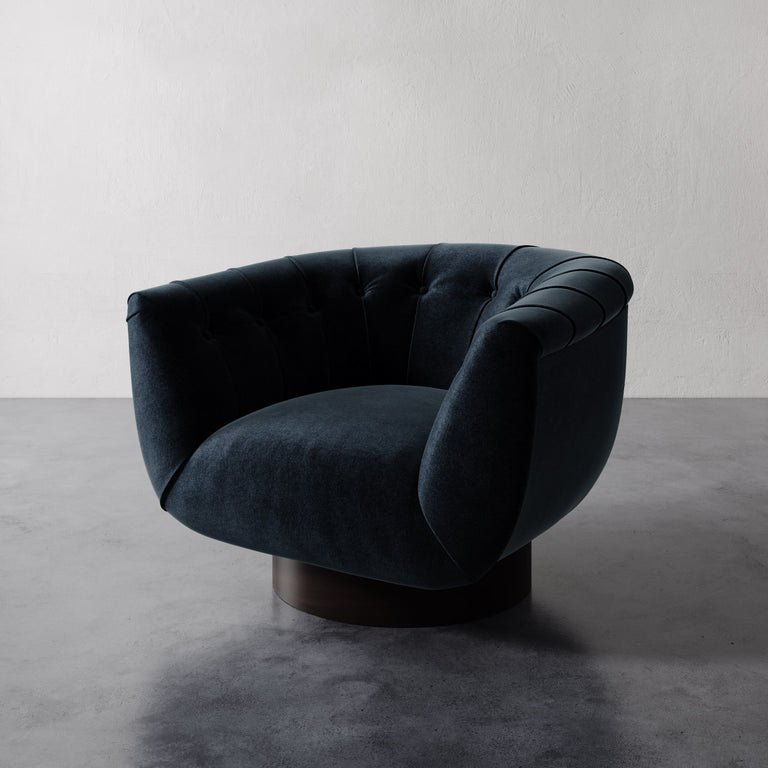 Indigo Lemieux et Cie Lune Swivel Chair with a rounded tufted back and sculptural form set against a white wall.