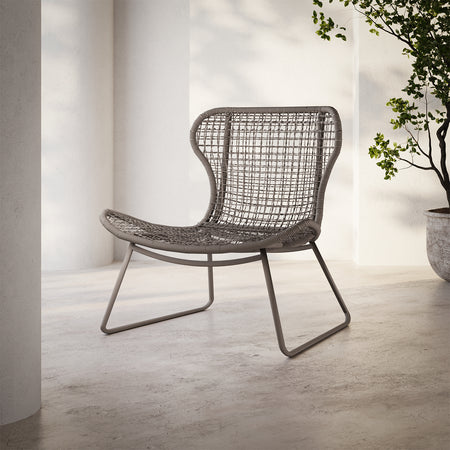 Lemieux et Cie Jagger Woven Lounge Chair with open-weave seat and back on sled base, shown on concrete floor near white columns and greenery.