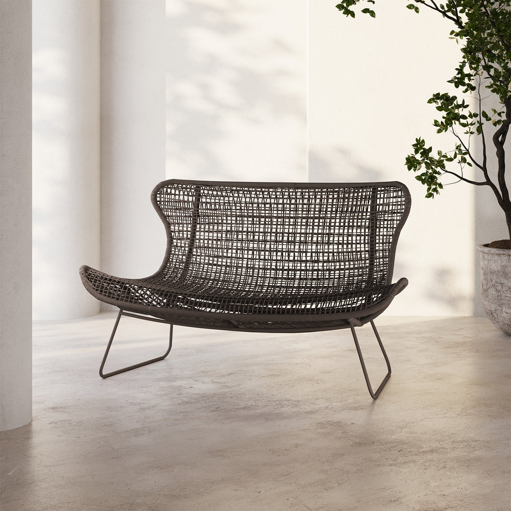 Lemieux et Cie Jagger Woven 65" Love Seat in dark woven all-weather finish with sculptural frame, outdoor loveseat on concrete floor in white-walled room with soft daylight.