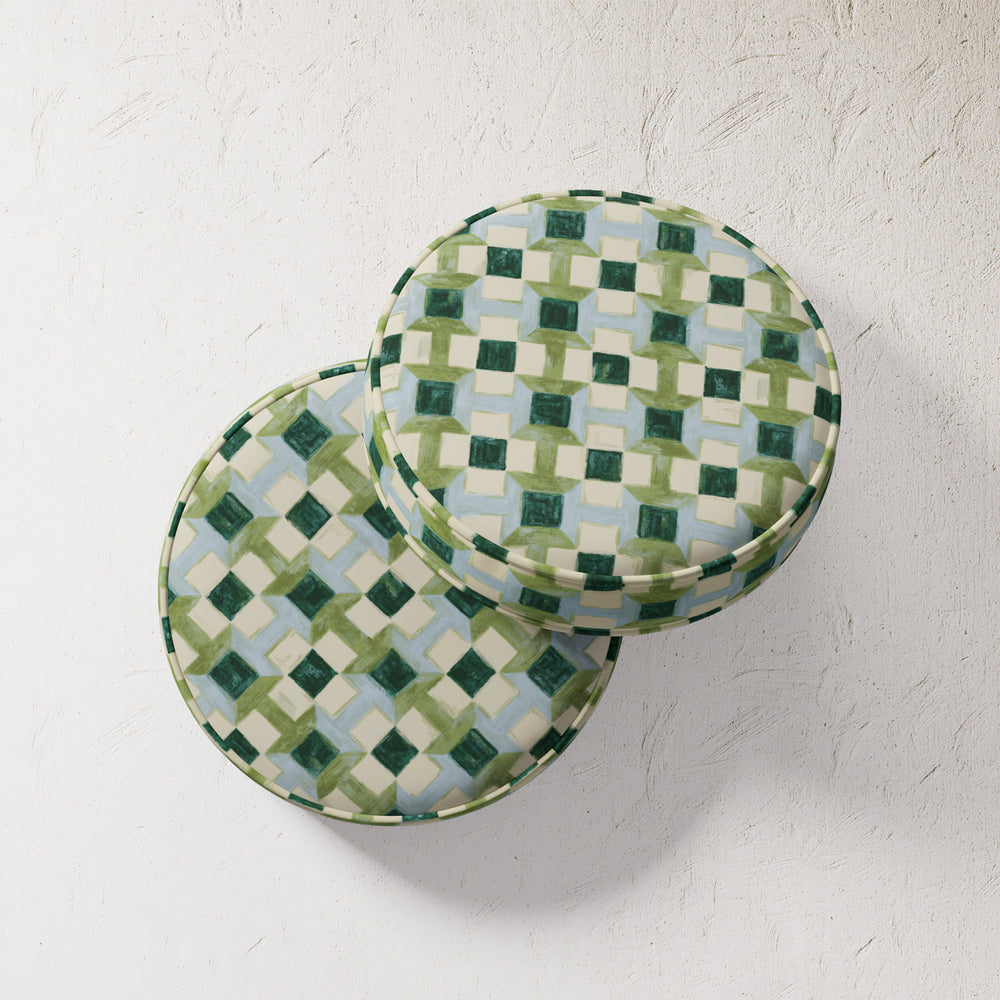 Lemieux et Cie Outdoor Pillow in geometric blue and green pattern, round throw pillows shown on textured plaster wall in soft light.