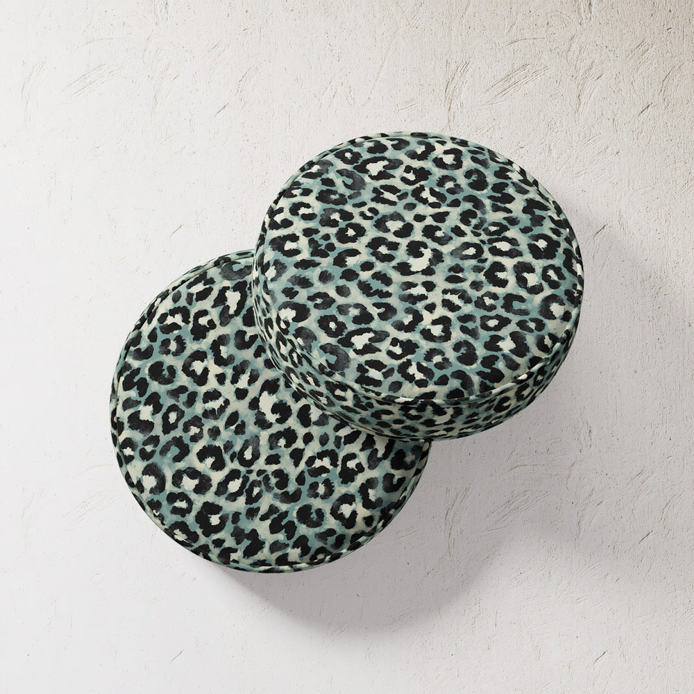 Lemieux et Cie Outdoor Pillow in teal leopard print, two round cushions stacked against textured plaster wall in soft natural light.