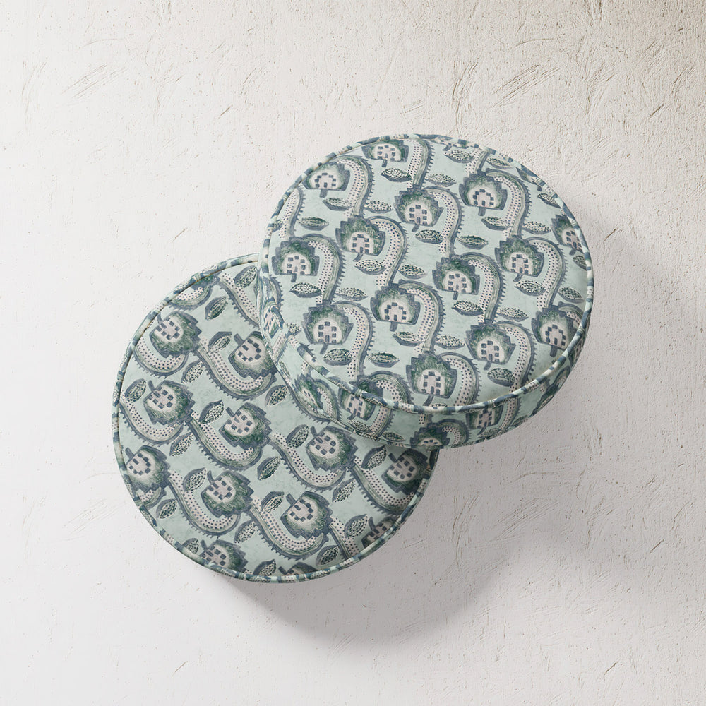Lemieux et Cie Outdoor Pillow in teal patterned upholstery, round cushion with geometric floral motif, shown on textured plaster wall.