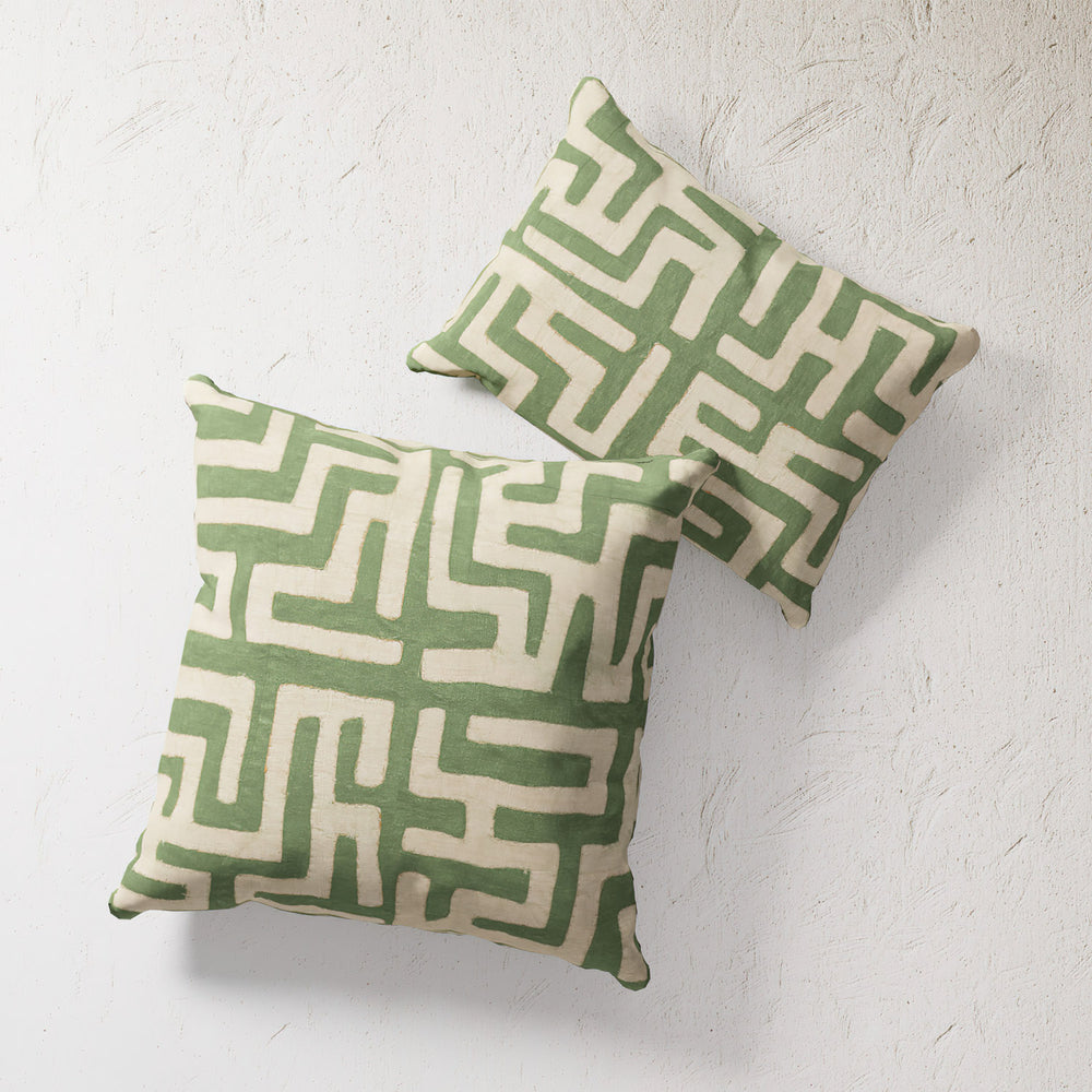 Lemieux et Cie Kuba Cloth Green Outdoor Pillow in geometric maze pattern, soft green and ivory, shown on textured plaster wall.
