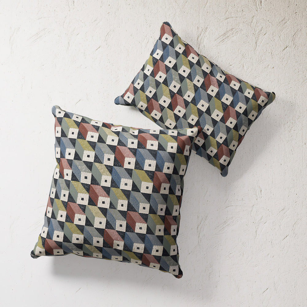 Lemieux et Cie Outdoor Pillow in Mosaic Cubes geometric pattern with blue, terracotta, olive and cream tones, shown on textured white plaster wall.