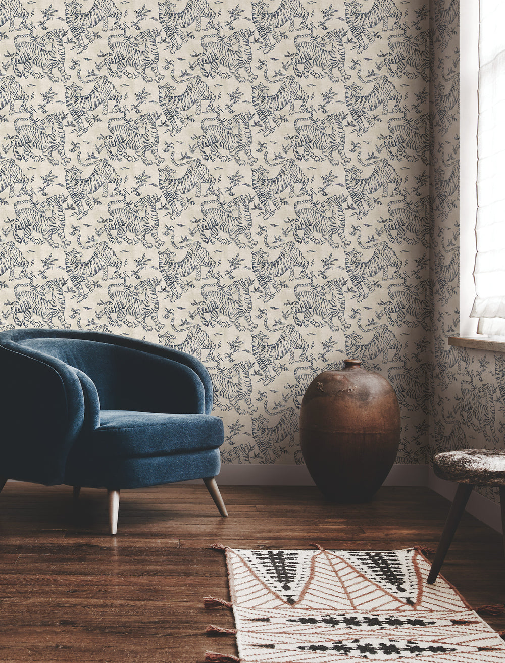 Lemieux et Cie Orly Tigers wallpaper in indigo blue on ecru, seated beside blue velvet chair and ceramic vase on wood floors.