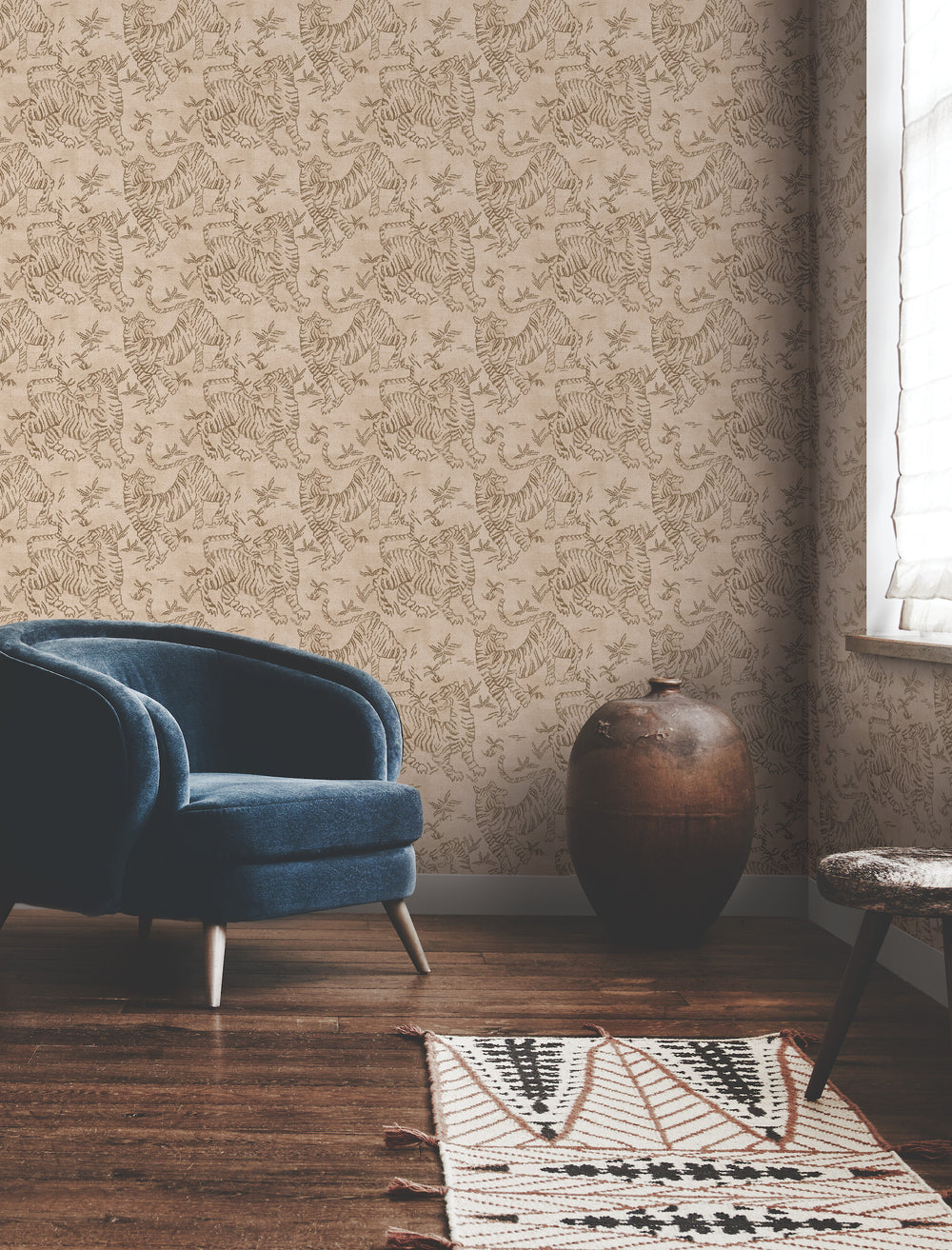 Lemieux et Cie Orly Tigers wallpaper in brown on blush pink, covering a sitting room wall beside a blue velvet chair and dark wood floors.