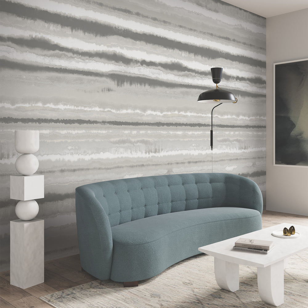 Lemieux et Cie Tachette wallcovering in soft taupe brown on white, watercolor brushstrokes behind curved tufted sofa and sculptural sconce in a neutral sitting room.
