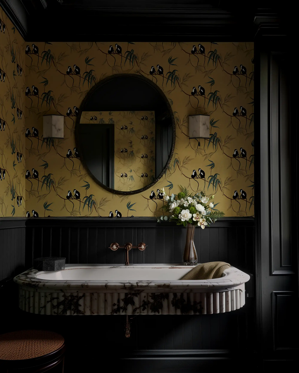 Lemieux et Cie Les Singes Wallpaper in golden ochre with monkeys and bamboo motif, chinoiserie pattern shown in powder room with dark paneled wainscoting and marble sink.