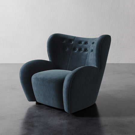 Lemieux et Cie Mondaine Lounge Chair in deep teal upholstery, sculptural wingback armchair with tufted back, on dark concrete floor against white walls.