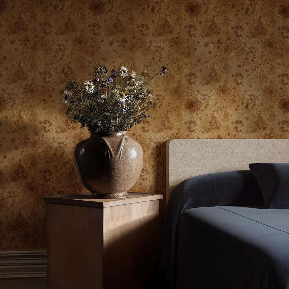 Lemieux et Cie Maison Mappa Burl Wood Wallpaper in blonde brown tones, peel and stick wallcovering with organic swirling grain, shown in sitting room with leather chair and dried botanicals.