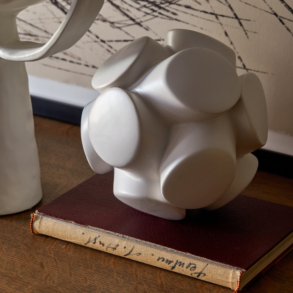 Lemieux et Cie Mayet Sphere Sculpture in white matte finish, geometric sculptural orb on vintage book atop wood table with marble backdrop.