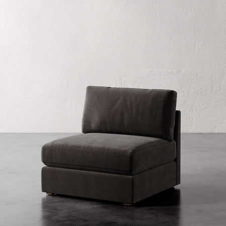 Lemieux et Cie Chanaux Armless Chair in charcoal upholstery, modular seating piece on dark concrete floor against textured white plaster wall.