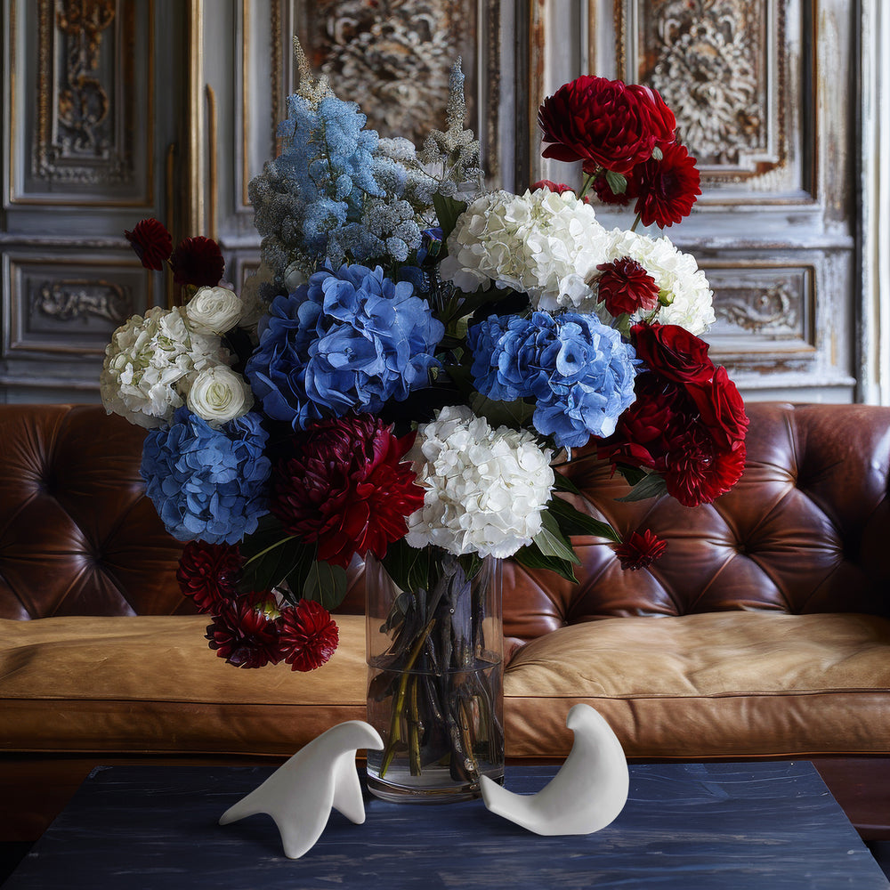 Lemieux et Cie bird objects in white ceramic, decorative doves displayed on navy blue table before a tufted leather sofa and carved wood paneling.