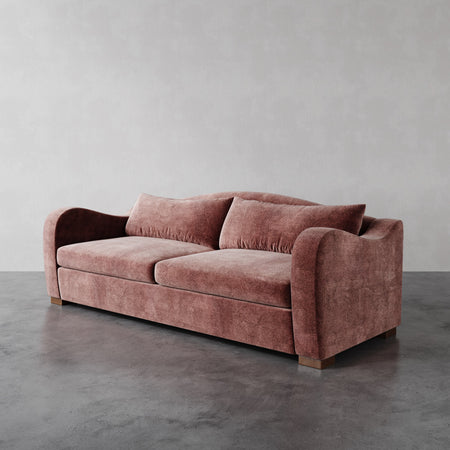 Lemieux et Cie Elodie Sofa in blush upholstery, deep-cushioned sofa with swooping arms and block feet, shown on polished concrete floor against white walls.
