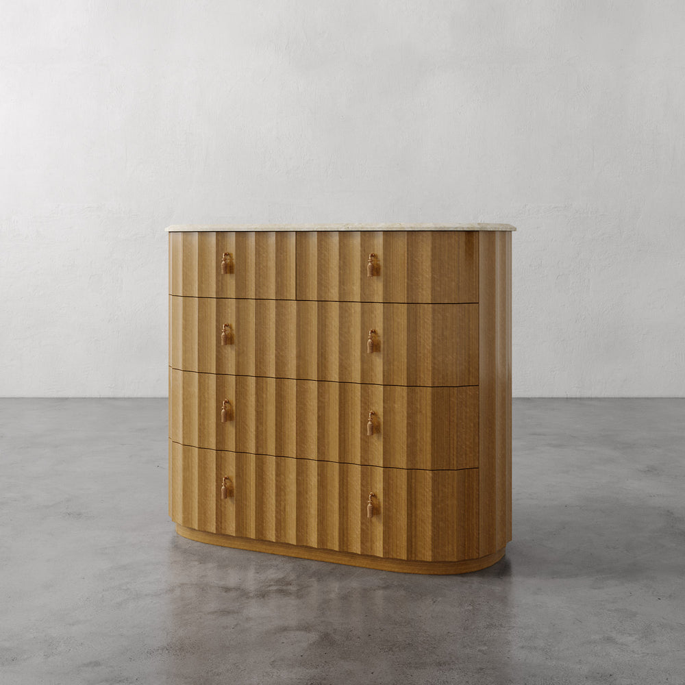 Lemieux et Cie Ondara Fluted 5-Drawer Dresser in champagne eucalyptus with honed travertine top and hand-cast brass pulls, shown on concrete floor against white walls.