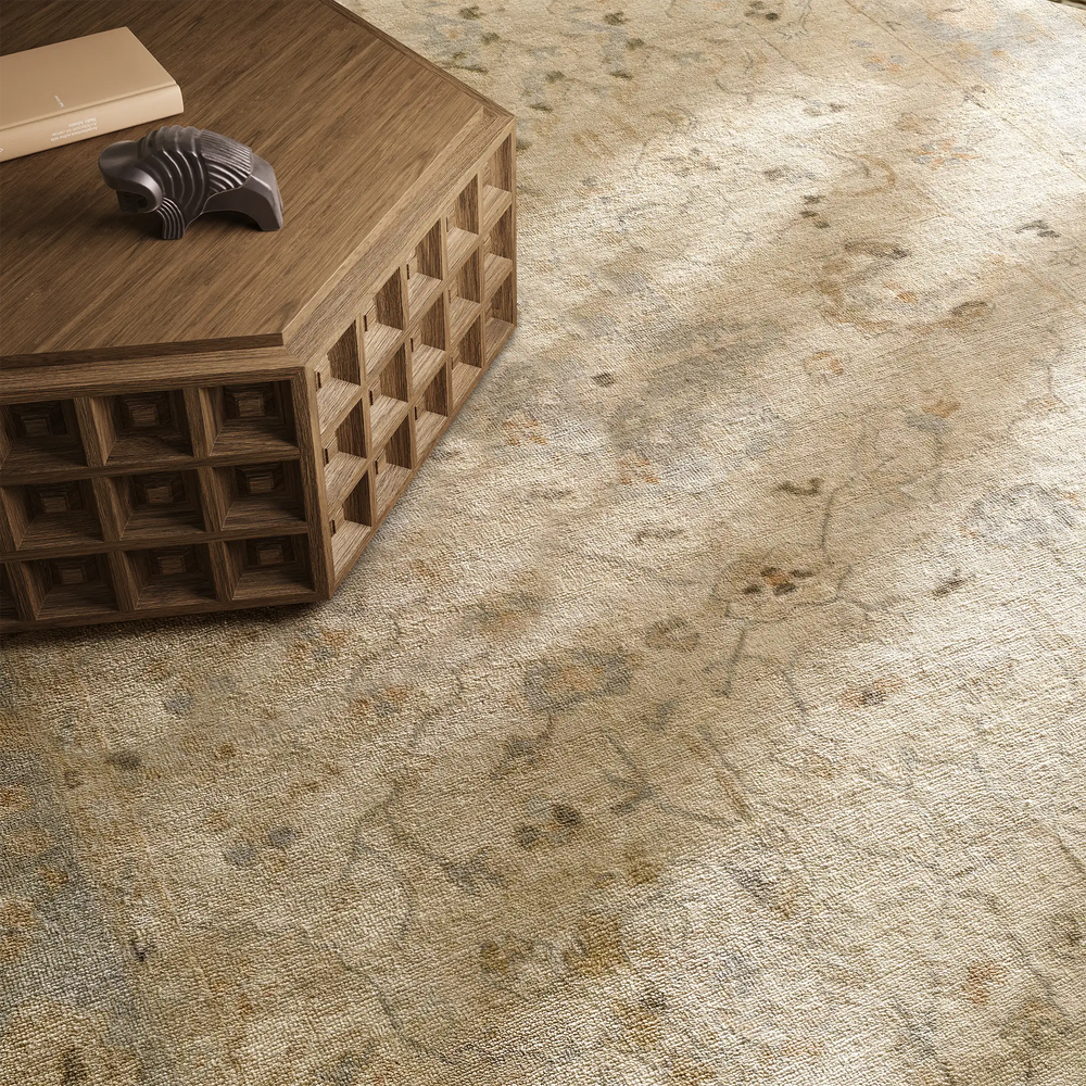 Lemieux et Cie Arabesque Fleurie handmade wool rug in neutral tones with subtle floral motif, shown beside geometric coffee table on wood floor.