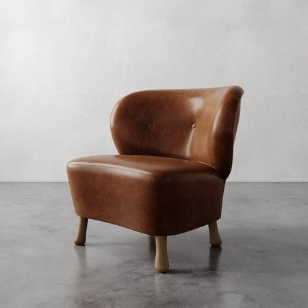 Lemieux et Cie Tourenne Chair in warm tobacco leather with rounded back and turned legs, slipper chair on polished concrete floor.