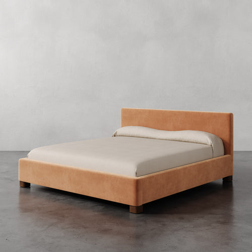 Lemieux et Cie Gérard Bed in warm blush upholstery, low-profile platform bed with wrapped headboard, styled with neutral linens on polished concrete floor.