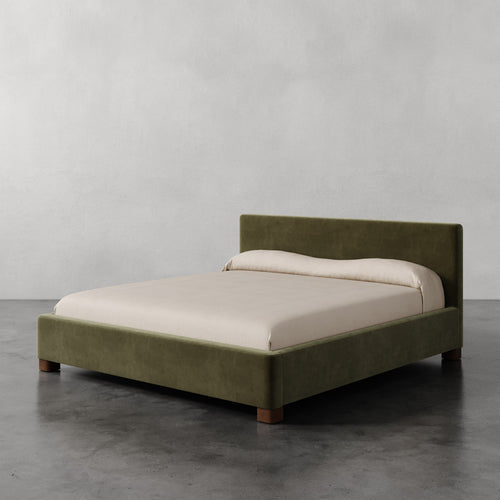 Lemieux et Cie Gérard Bed in olive green upholstery, low-profile platform bed with neutral linen bedding, shown on polished concrete floor against white walls.