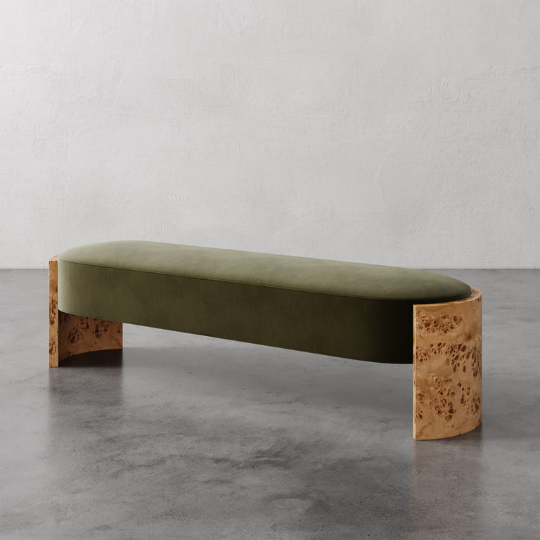 Lemieux et Cie Benoit Custom Upholstered Bench with olive velvet cushion and curved Maple burl legs, shown on concrete floor against white textured walls.