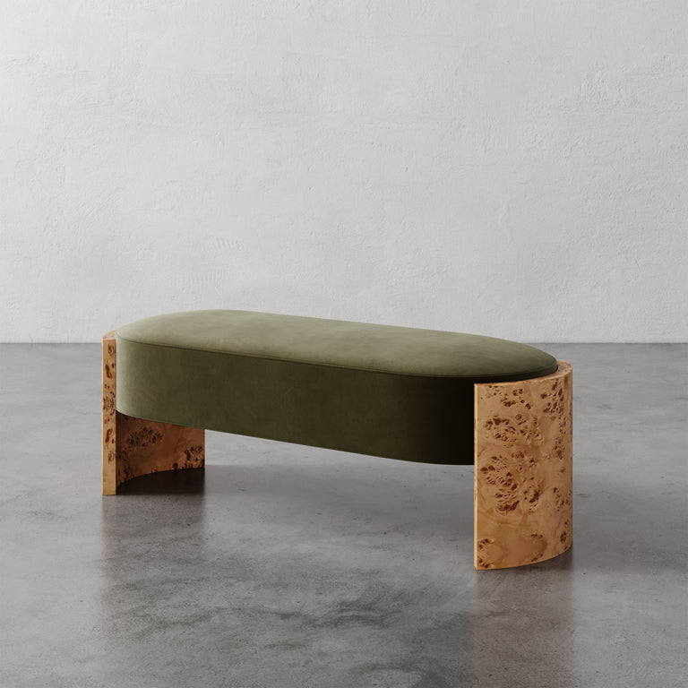 Lemieux et Cie Benoit Bench with olive green upholstered seat and curved Maple burl legs, shown on polished concrete floor against textured plaster walls.