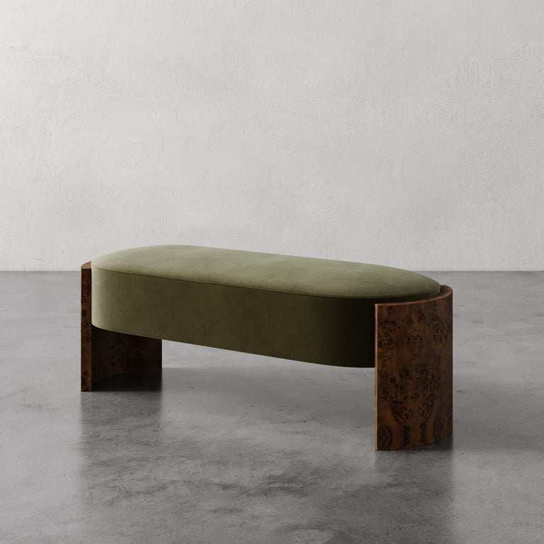 Lemieux et Cie Benoit Bench with olive upholstered seat and curved Maple burl legs, shown on polished concrete floor against textured plaster walls.