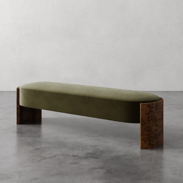 Lemieux et Cie Benoit Custom Upholstered Bench in olive velvet with curved Maple burl legs, shown on polished concrete floor against textured plaster walls.