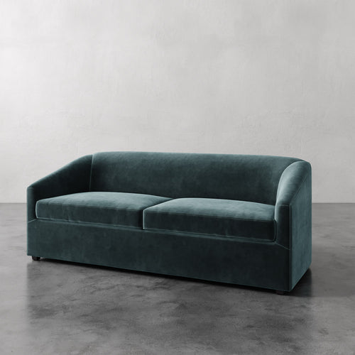 Lemieux et Cie Arvelle Queen Sleeper in deep teal, curved-arm sofa shown on polished concrete floor against neutral plaster wall.