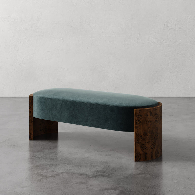 Lemieux et Cie Benoit Custom Upholstered Bench in teal velvet with curved Maple burl legs, shown on polished concrete floor against textured plaster walls.