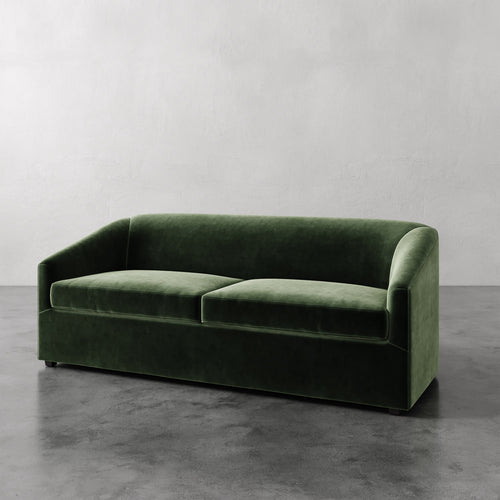 Lemieux et Cie Arvelle Queen Sleeper in deep green velvet, low-profile sofa with curved arms shown on polished concrete floor against white walls.