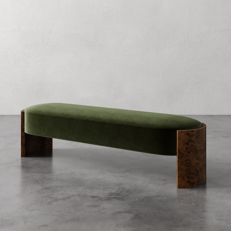 Lemieux et Cie Benoit Bench in olive velvet with curved Maple burl legs, upholstered bench on polished concrete floor against textured plaster walls.