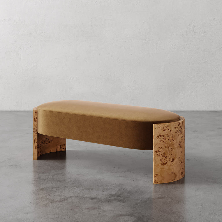 Lemieux et Cie Benoit Custom Upholstered Bench in camel velvet with curved Maple burl legs, shown on polished concrete floor against textured plaster wall.