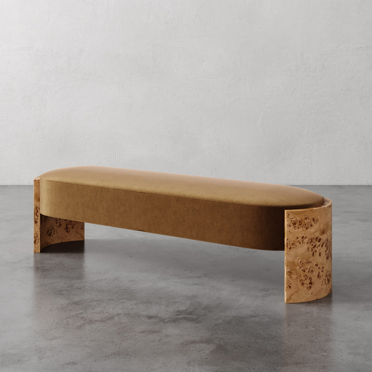 Lemieux et Cie Benoit Custom Upholstered Bench in warm tan fabric with curved Maple burl legs, shown on polished concrete floor against textured plaster walls.