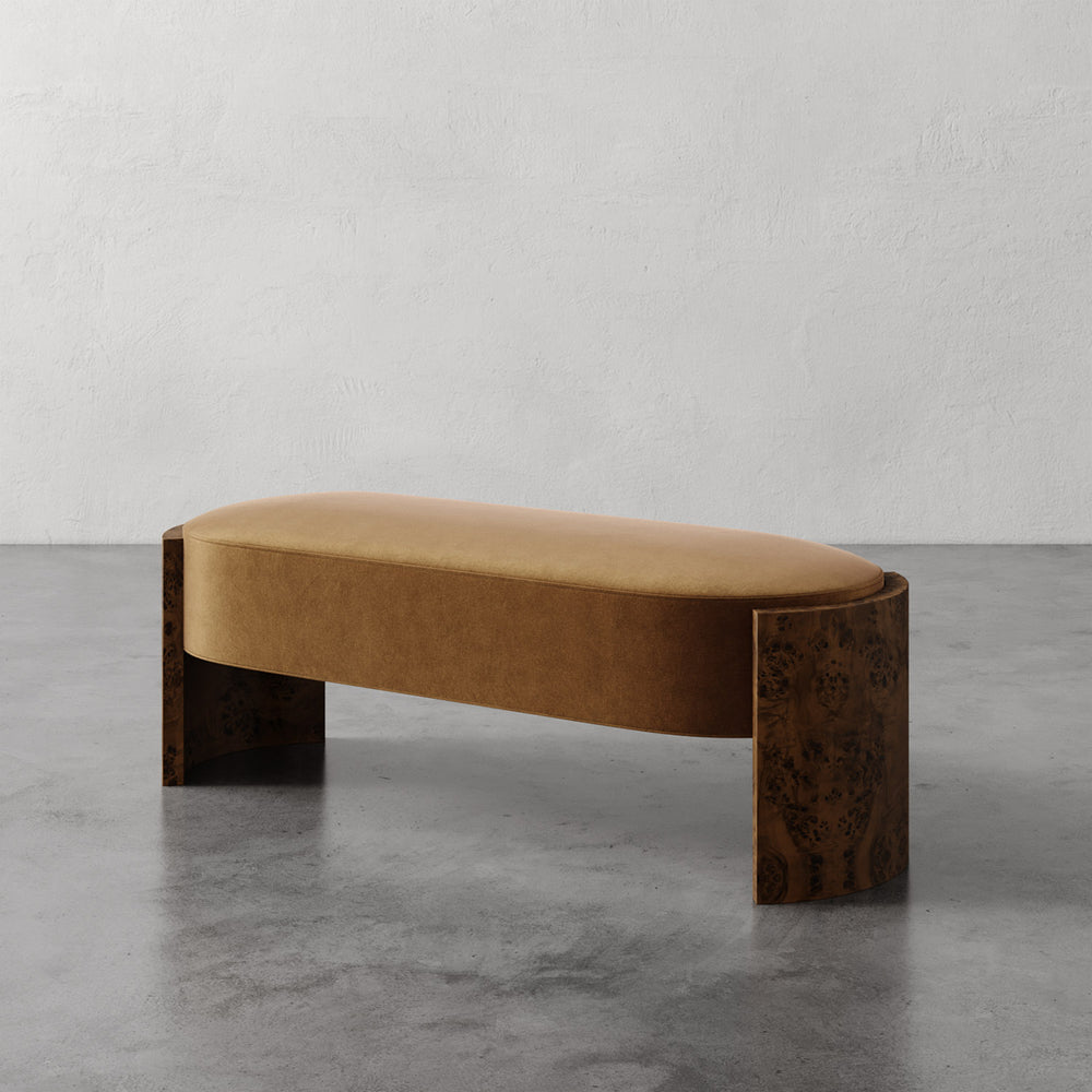 Lemieux et Cie Benoit Bench in warm upholstery with curved Maple burl legs, custom upholstered bench on concrete floor against textured plaster walls.