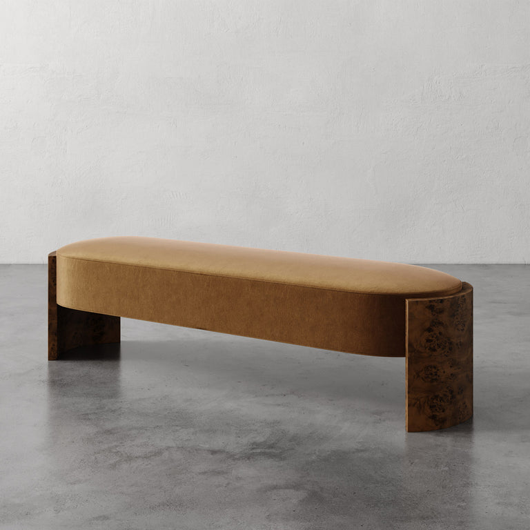 Lemieux et Cie Benoit Custom Upholstered Bench with curved maple burl legs and warm upholstered seat, shown on polished concrete floor against white wall.