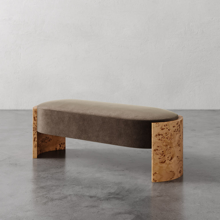 Lemieux et Cie Benoit Custom Upholstered Bench with curved Maple burl legs and taupe velvet seat, shown on concrete floor against white plaster wall.