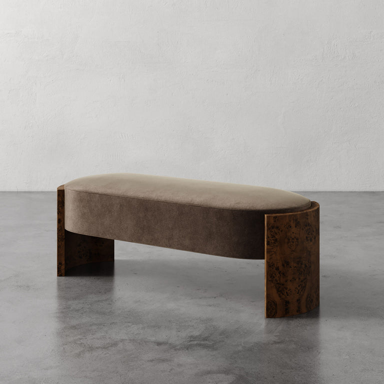 Lemieux et Cie Benoit Custom Upholstered Bench with curved Maple burl legs and upholstered seat in warm taupe, shown on concrete floor against textured plaster walls.