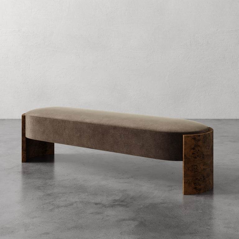 Lemieux et Cie Benoit Custom Upholstered Bench in taupe velvet with curved Maple burl legs, shown on polished concrete floor against textured plaster wall.