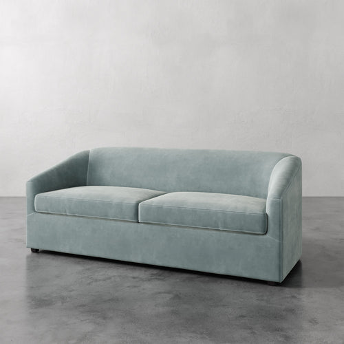 Lemieux et Cie Arvelle Queen Sleeper in soft sage blue, low-profile sofa with rounded arms, shown on polished concrete floor against neutral walls.