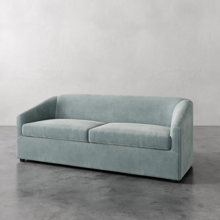 Lemieux et Cie Arvelle Queen Sleeper in soft sage blue, low-profile sofa with rounded arms, shown on polished concrete floor against neutral walls.