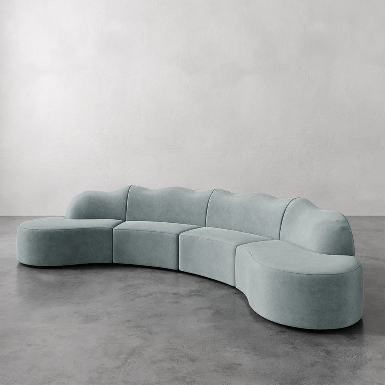 Lemieux et Cie Serpentine Sectional Sofa in pale sage, curved modular seating on concrete floor against neutral plaster walls.