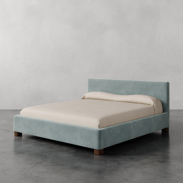 Lemieux et Cie Gérard Bed, low-profile platform bed with wrapped headboard and block feet, shown on polished concrete floor against neutral plaster walls.