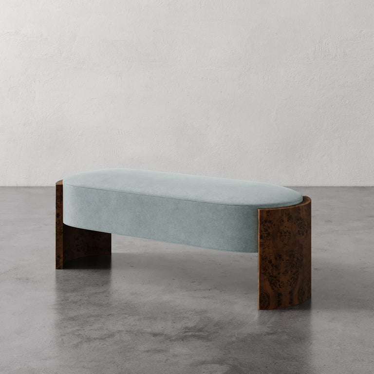 Lemieux et Cie Benoit Custom Upholstered Bench in pale blue with curved Maple burl legs, shown on polished concrete floor against textured plaster walls.